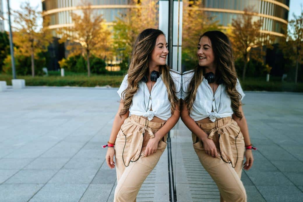 Joven mujer sonriente reflejada en espejo mostrando cómo tener más confianza y seguridad en uno mismo
